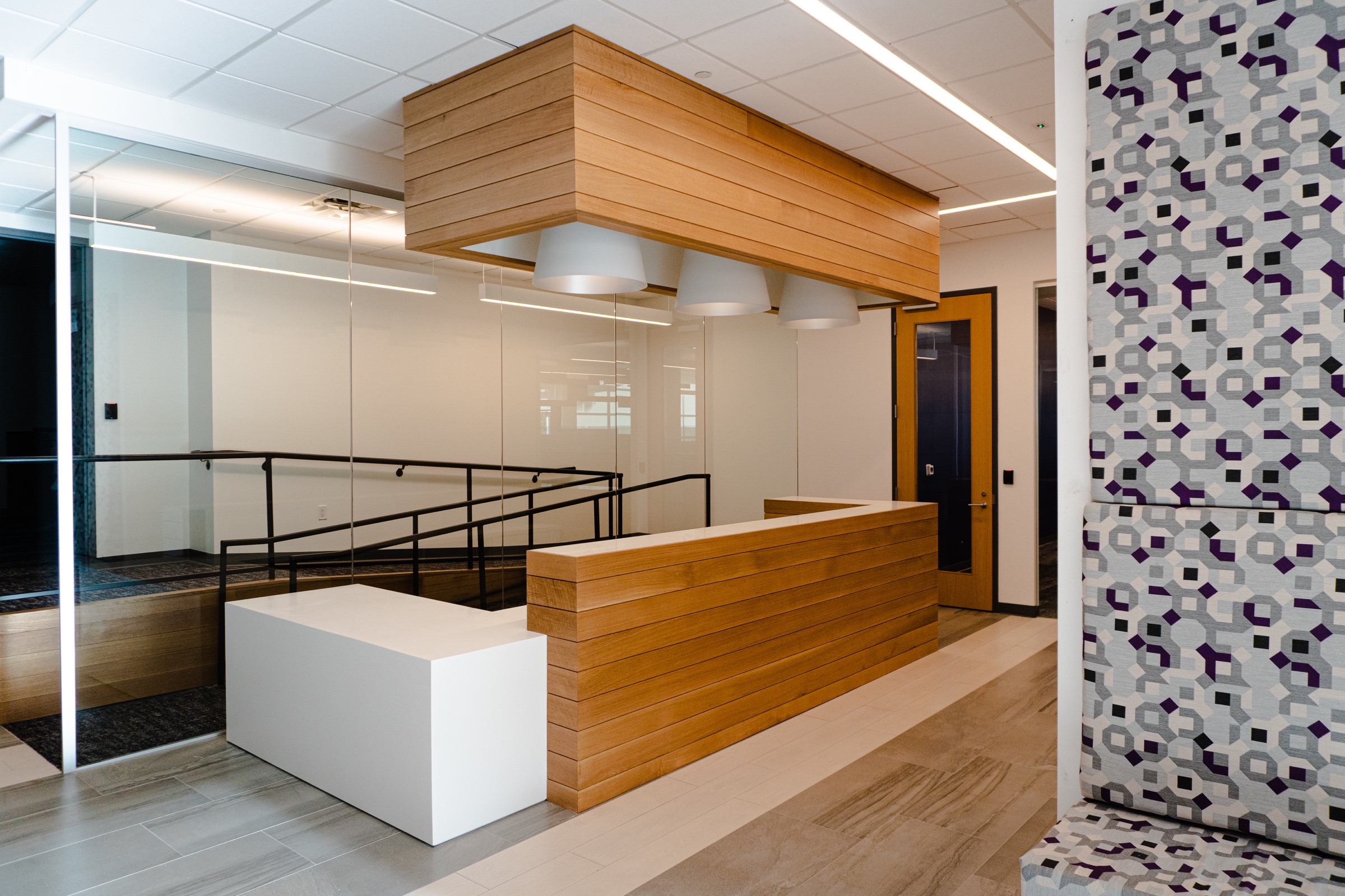 Finished reception area with slatted wood millwork, a full-height glass partition and a patterned acoustic wall panel
